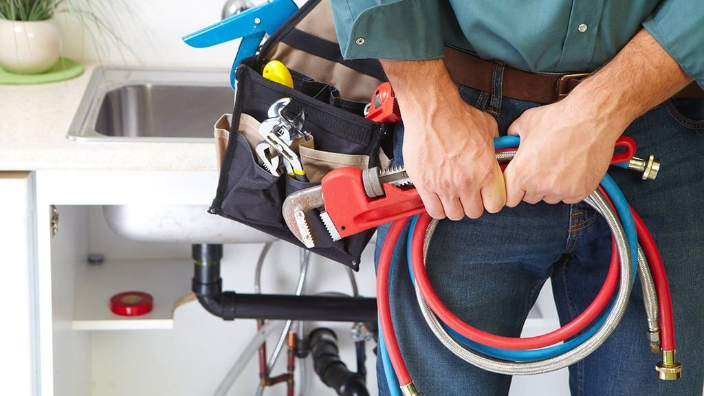 A plumber with tools and supply lines at a kitchen sink